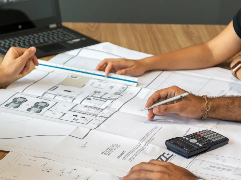 Two people reviewing printed architectural floor plans with a pencil and calculator